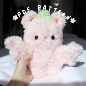 Puede incluir: Un peluche rosa con forma de oso con una parte superior verde y ojos negros. El oso tiene los brazos extendidos y está hecho de un material suave y esponjoso. El texto "PDF PATTERN" está escrito encima del oso.