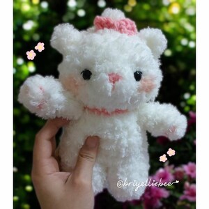 May include: A handmade white teddy bear with a pink bow, nose, and blush. The bear has black eyes and a pink stitched mouth. The bear is made of a soft, fluffy material. The bear is approximately 6 inches tall.