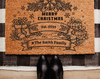May include: A rectangular coir doormat with a black and brown design. The mat features the text "MERRY CHRISTMAS" above a banner that reads "Est. 2025" and "The Smith Family". The design includes Christmas bells, gifts, and snowflakes.