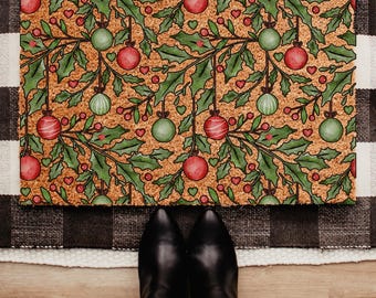 May include: A rectangular doormat with a festive Christmas design. The mat features a repeating pattern of red and green ornaments, holly leaves, and red hearts on a textured brown background. The border is a black and white checkered pattern.