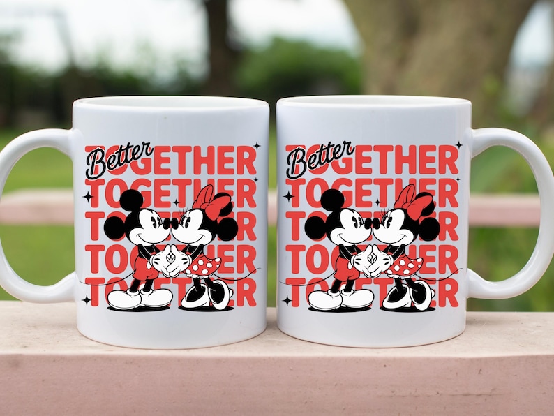 Op de afbeelding: Twee witte keramische mokken met de woorden "Better Together" in rood en zwart. Elke mok heeft een afbeelding van Mickey en Minnie Mouse die elkaar omarmen. Perfect voor koppels of Disney-fans.