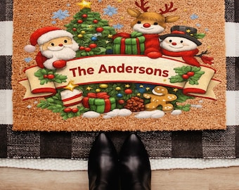 May include: A rectangular doormat with a Christmas theme. The mat features Santa Claus, a reindeer, and a snowman, along with a Christmas tree and gifts. The text "The Andersons" is displayed on a banner. The mat is brown with a black and white checkered border.