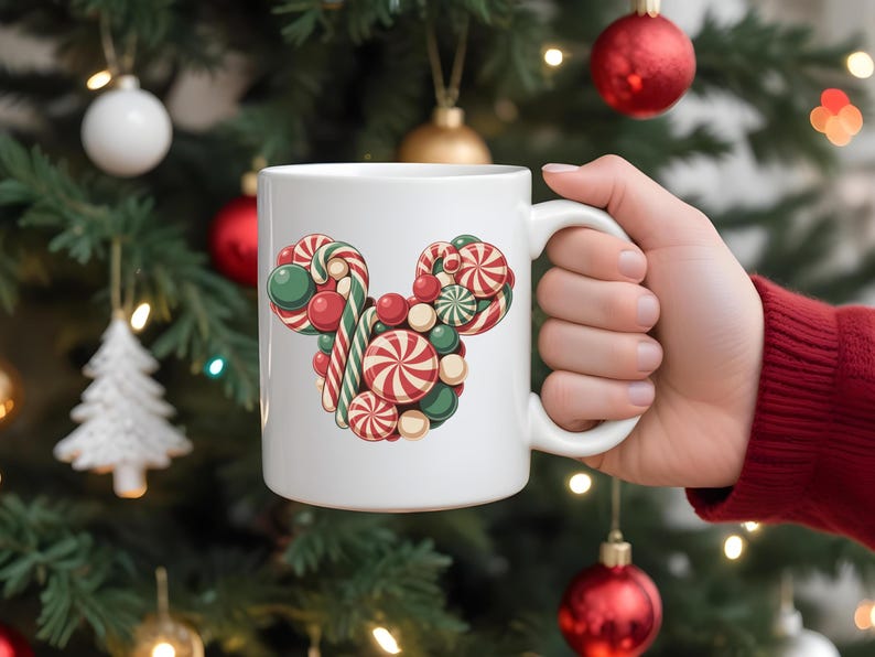 Puede incluir: Taza de cer&aacute;mica blanca con un dise&ntilde;o de caramelos en forma de cabeza de rat&oacute;n. El dise&ntilde;o incluye caramelos rojos, verdes y blancos. La taza se sostiene frente a un &aacute;rbol de Navidad.