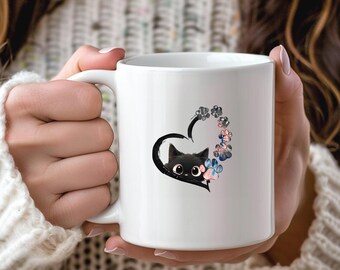May include: White ceramic mug featuring a black cat peeking out of a black heart. The heart is surrounded by paw prints in shades of pink, blue, and gray. The mug has a white handle.