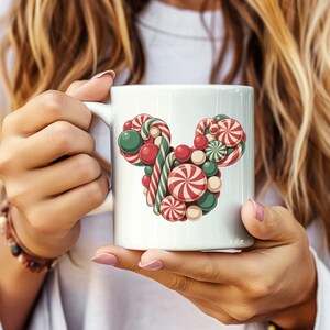 Puede incluir: Taza de cer&aacute;mica blanca con un dise&ntilde;o colorido de caramelos dispuestos en forma de cabeza de rat&oacute;n. El dise&ntilde;o incluye caramelos rojos, verdes y blancos, incluyendo espirales de menta y bastones de caramelo. La taza es sostenida por una persona.