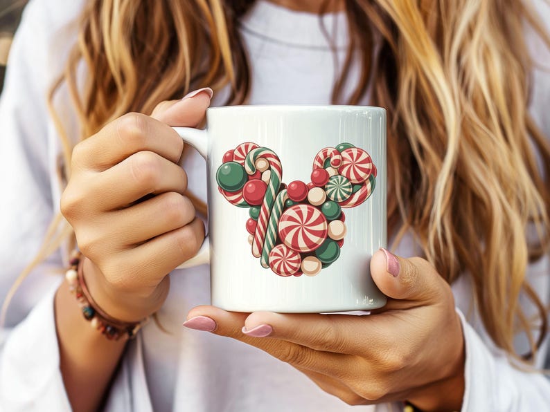 Puede incluir: Taza de cer&aacute;mica blanca con un dise&ntilde;o colorido de caramelos dispuestos en forma de cabeza de rat&oacute;n. El dise&ntilde;o incluye caramelos rojos, verdes y blancos, incluyendo espirales de menta y bastones de caramelo. La taza es sostenida por una persona.