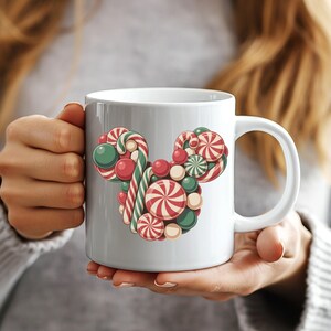 Puede incluir: Taza de cer&aacute;mica blanca con un dise&ntilde;o festivo de una cabeza de Mickey Mouse hecha de caramelos. El dise&ntilde;o incluye bastones de caramelo a rayas rojas y blancas, caramelos redondos verdes y rojos y caramelos en espiral rojos y blancos.