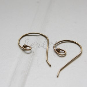 Könnte beinhalten: Zwei goldfarbene Ohrhaken mit einer kleinen Kugel an der Spitze jedes Hakens.