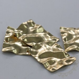 Puede incluir: Cuatro cuadrados de metal de color dorado con una superficie ondulada y texturizada. Cada cuadrado tiene un pequeño agujero en el centro.