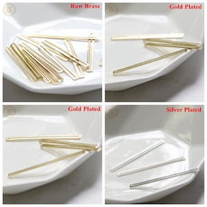 May include: Four white dishes containing gold, silver, and brass metal bar shapes. The dishes are labelled "Raw Brass", "Gold Plated", "Gold Plated", and "Silver Plated".