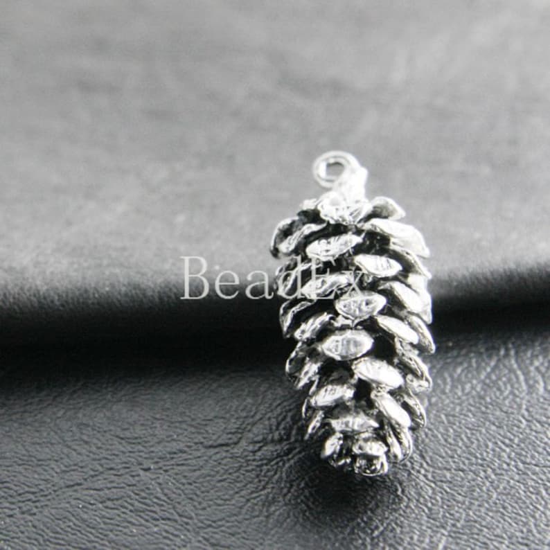 May include: Silver-toned metal pine cone charm with a loop at the top for attaching to jewelry or crafts.