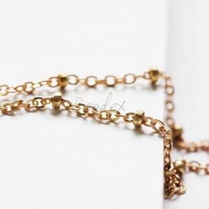 May include: A gold chain necklace with small round beads. The chain is delicate and has a subtle shine.