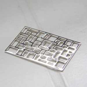 May include: Silver metal pendant with a geometric design of squares and rectangles. The pendant is a flat, rectangular shape with a grid pattern.