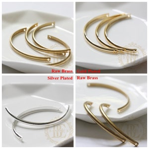 May include: Three metal bangle bracelets in different finishes: raw brass, gold plated, and silver plated. The bracelets are all the same size and shape, with a slightly curved design.