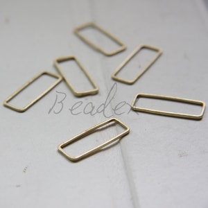 May include: Five gold-colored metal rectangular jump rings. The rings are scattered on a white surface.