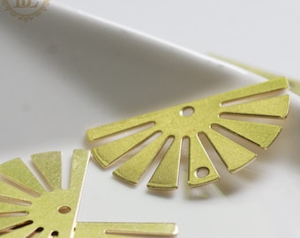 May include: Close-up of several brass-colored sunburst charms. Each charm has a half-circle shape with multiple rays extending outward. The charms have small holes for stringing or attaching to other jewelry components. The background is a white surface.