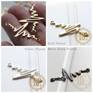 May include: Four heart-shaped metal charms in different finishes: raw brass, gold plated, silver plated, and matte black plated. Each charm features a wavy line design.