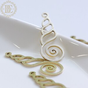 Puede incluir: Tres piezas decorativas de metal dorado con un diseño en espiral. Las piezas están recortadas y tienen un diseño delicado e intrincado.