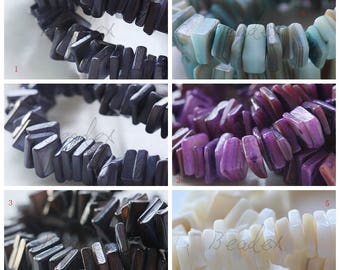 Op de afbeelding: Assortiment van 10 mm schelp kralen in verschillende kleuren, waaronder zwart, blauw, paars en wit. De kralen zijn rechthoekig en hebben een plat, gepolijst oppervlak.