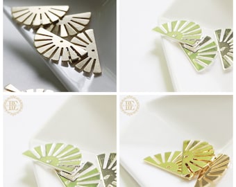 May include: Four gold-colored metal sunburst shapes, each with a fan-like design, are arranged on a white surface. The shapes are approximately 2 inches in diameter.