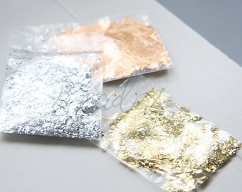 Può includere: Tre piccoli sacchetti di scaglie di foglia metallica. I sacchetti sono di plastica trasparente e le scaglie sono argentate, dorate e oro rosa.