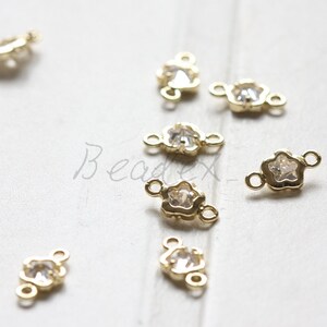 Könnte beinhalten: Goldfarbener Metall-Blumenverbinder mit einem klaren Strassstein in der Mitte. Der Verbinder hat zwei Sprungringe zum Anbringen an Schmuck.