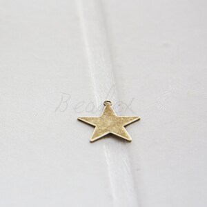 Könnte beinhalten: Ein goldfarbener Metall-Stern-Anhänger mit leicht abgenutzter Oberfläche. Der Stern hat oben eine Öse zum Anbringen an Schmuck oder anderen Bastelarbeiten.
