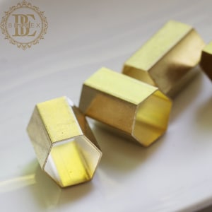 May include: Four gold-colored hexagonal rings, stacked on top of each other, on a white surface.