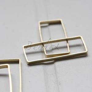 May include: Two gold metal rectangular frames, one slightly larger than the other, are stacked on top of each other. The frames are open on all sides.