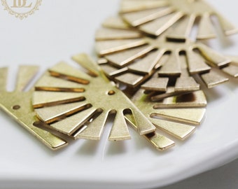 May include: Close-up of several brass-colored metal leaf-shaped components. Each component has a central stem with radiating lines, resembling a stylized fan or leaf. The components are arranged on a white surface.