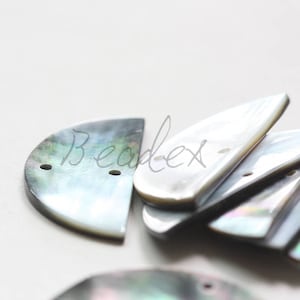 May include: A close-up of a stack of iridescent, half-moon shaped shell buttons with two holes each. The buttons are a mix of white and black with a pearlescent sheen.