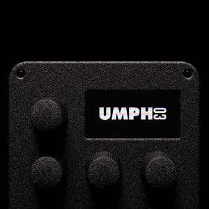 May include: A close-up shot of a black electronic device featuring the text "UMPH03" on a small screen. The device has textured knobs and a rectangular form, set against a dark backdrop.