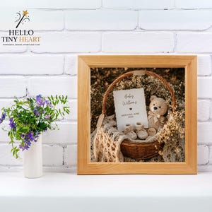 Rustic baby announcement basket featuring a plush teddy bear, cream knit booties, baby's breath flowers, and a card reading "Baby Williams Arriving June 2026" on a beige macrame blanket.