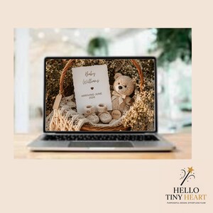 May include: A laptop screen displays a baby announcement with the text "Baby Williams ARRIVING JUNE 2026." The announcement is in a wicker basket with a teddy bear and baby shoes. The laptop is on a wooden surface.