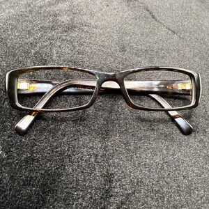 May include: Rectangular eyeglasses featuring a dark brown and black tortoiseshell pattern frame. The temples are visible behind the front rims, and the inner arm displays the text Made in Italy and the model number AU-101 135 in white print.