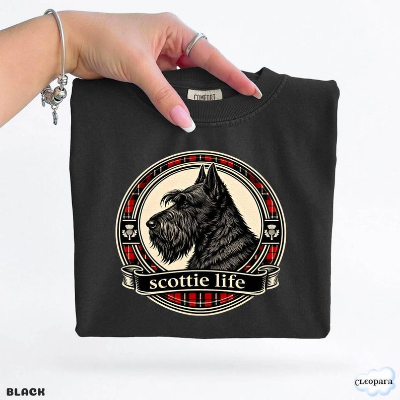 May include: Black crew neck sweatshirt featuring a circular graphic of a Scottish Terrier dog with the text "scottie life" on a banner. The graphic is framed by a red and black plaid pattern. The word "BLACK" is at the bottom left.