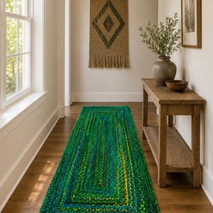 Puede incluir: Una alfombra de pasillo trenzada rectangular que presenta una mezcla vibrante de tonos esmeralda, verde bosque, lima y azul profundo. La alfombra está construida con un patrón rectangular concéntrico, mostrando un tejido grueso y texturizado.