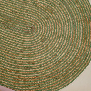 Può includere: Tappeto ovale in juta con un motivo a righe verdi e naturali. Il design del tappeto presenta linee curve concentriche, creando una superficie strutturata. Il tappeto è realizzato con fibre naturali e ha una palette di colori neutri.