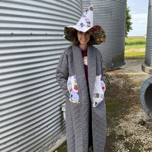 May include: A gray quilted coat with colorful patchwork pockets and a matching patchwork witch hat. The hat has a wide brim and a tall, pointed crown. The coat is long and has a quilted pattern.