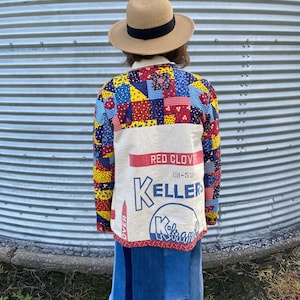 May include: A long-sleeve jacket featuring a patchwork upper section with colorful floral and geometric patterns, and a lower section made from a cream-colored fabric printed with the text RED CLOVER, CR-520, KELLERS, and K-brand.
