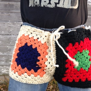 May include: A crocheted granny square belt with a white, orange, blue, black, red, and green color scheme. The belt is tied at the front with a white string.