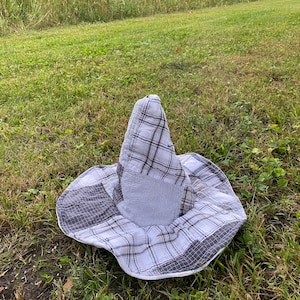 May include: A pointed hat constructed from various fabric patches in shades of white, gray, and black. The hat features a mix of plaid, checkered, and pinstriped patterns throughout its conical crown and wide, flexible brim, creating a patchwork design.