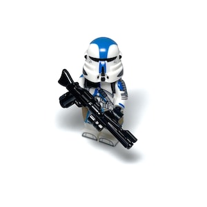 Może przedstawiać: Minifigurka Lego Star Wars przedstawiająca żołnierza-klona, z białym i niebieskim hełmem i zbroją. Figurka trzyma czarny karabin blaster. Tło jest jednolicie białe.