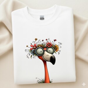 K&ouml;nnte beinhalten: Wei&szlig;es Sweatshirt mit einer skurrilen Flamingo-Illustration. Der Flamingo hat eine gro&szlig;e, runde Brille und einen Blumenkranz. Der Vogel ist orange mit einem schwarzen Schnabel, vor wei&szlig;em Hintergrund.