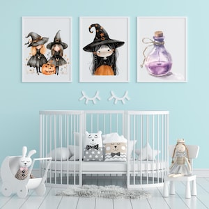 May include: Three framed watercolor prints with a Halloween theme. The prints feature illustrations of witches, a potion bottle, and a pumpkin. The prints are displayed above a white crib with decorative pillows and a toy stroller.