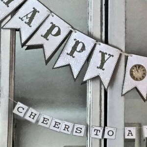 Puede incluir: Una pancarta blanca y gris con las palabras "Happy New Year" y "Cheers to a New Year" colgada en una puerta de madera blanca con espejos. La pancarta tiene un diseño de esfera de reloj en algunas de las banderas.