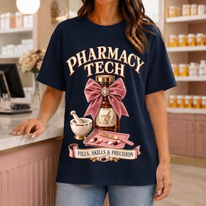 May include: A navy blue t-shirt featuring the text PHARMACY TECH in a cream font. The graphic includes an amber medicine bottle with a pink velvet bow, a mortar and pestle, a tray with pills and a spatula, and the text PILLS, SKILLS & PRECISION.