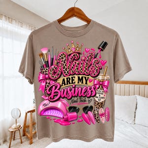 Peut inclure: Un t-shirt beige avec une impression graphique portant le texte "Nails Are My Business Nail Tech". Le motif comprend une couronne à motif léopard, des pinceaux, une lampe à ongles rose, un gobelet à café, des lunettes et des vernis roses.