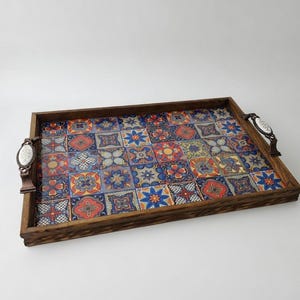 May include: A rectangular wooden serving tray with a colorful tile design. The tray features a dark wood frame and decorative handles with white and brown accents. The tile pattern includes blue, orange, and yellow floral motifs.