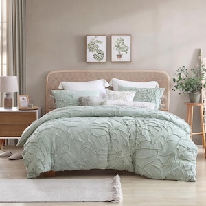 Puede incluir: Un juego de cama verde salvia con un patrón abstracto texturizado en relieve en la funda nórdica y fundas de almohada a juego. El conjunto incluye cojines blancos y se muestra en una cama con un cabecero de rejilla de color marrón claro.